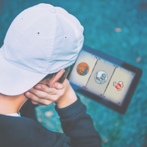 Kind mit einem Basecap schaut auf ein Tablet, auf dem mehrere Symbole von LOVE Storm zu sehen sind. Die Person ist von hinten zu sehen und die Symbole verschwommen.